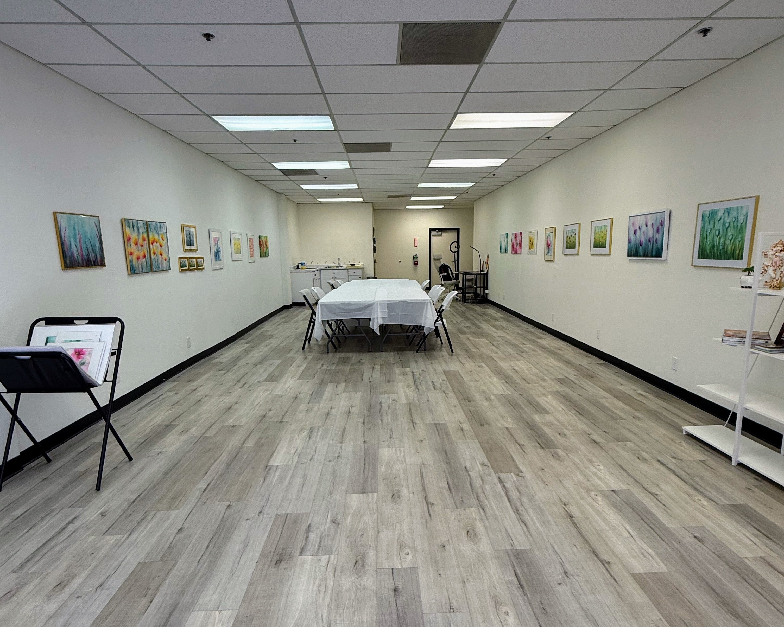 Long room with wooden flooring and white walls, featuring tables and chairs.